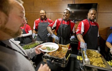 Atlanta Falcons' Justin Blalock, Jonathan Massaquoi and Corey Peters, from left, serve an early Thanksgiving dinner to Ronnie Fowler, left, and about 100 other men from Shepherd's Inn, the men's facility at the Atlanta Mission, Monday, Nov. 25, 2013, in Atlanta. The Falcons players served the catered meal at the mission which provides overnight shelter and transitional housing for more than 950 homeless men, women and children daily. (AP Photo/David Goldman)